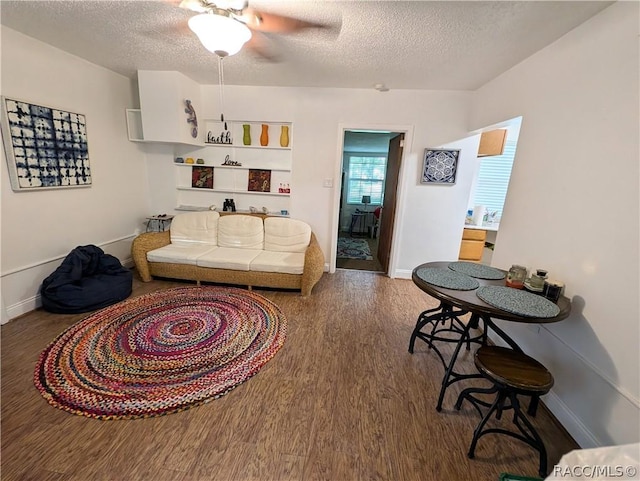 living area featuring a textured ceiling, baseboards, and wood finished floors