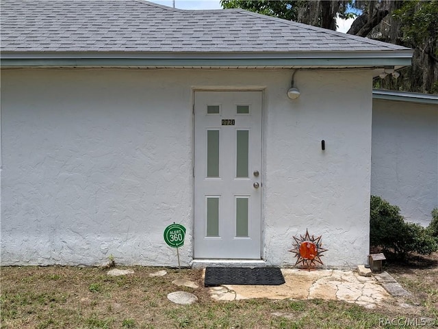 entrance to property with a shingled roof and stucco siding