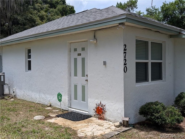 view of exterior entry featuring a shingled roof and stucco siding