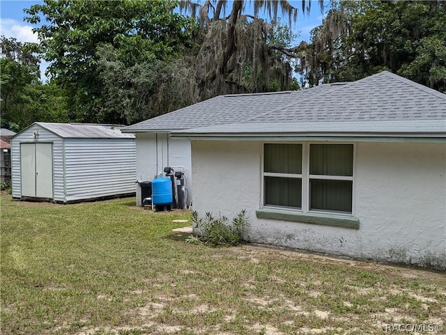 view of home's exterior with roof with shingles, a yard, stucco siding, a shed, and an outdoor structure