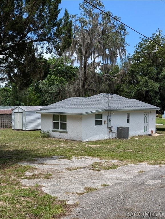 view of side of home with a lawn, central AC unit, and a shed