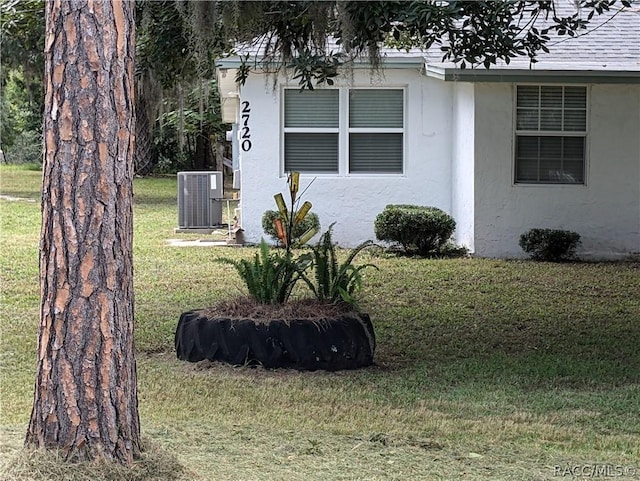 view of side of property with a yard, roof with shingles, central AC unit, and stucco siding