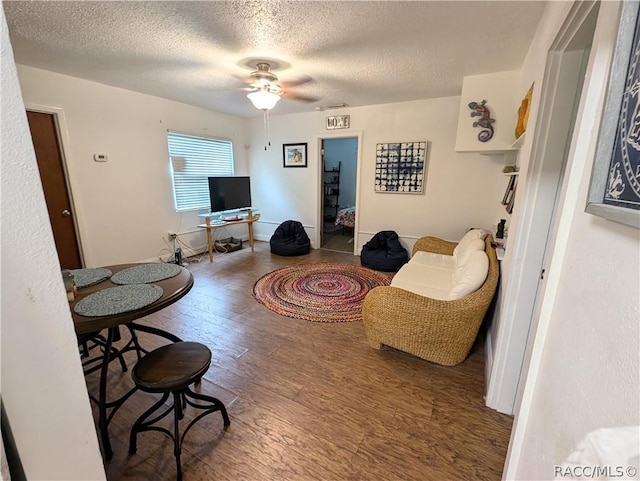 living area featuring a textured ceiling, ceiling fan, hardwood / wood-style floors, and baseboards