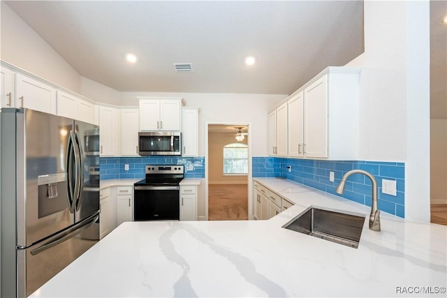 kitchen featuring decorative backsplash, appliances with stainless steel finishes, light stone counters, sink, and white cabinets