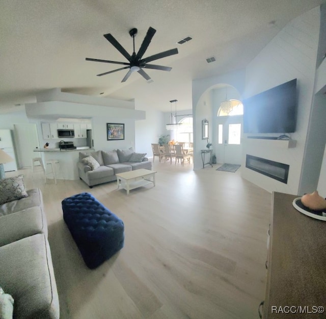 living room with a textured ceiling, light hardwood / wood-style flooring, ceiling fan, and lofted ceiling