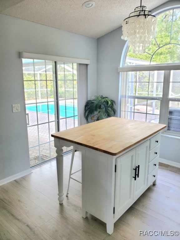 kitchen with pendant lighting, a center island, a textured ceiling, white cabinetry, and butcher block counters