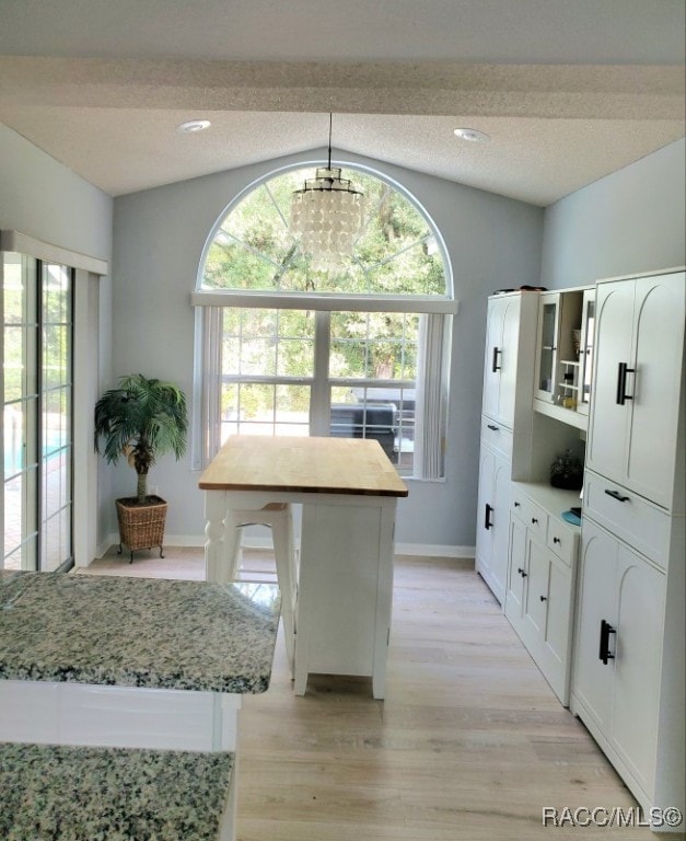 kitchen with white cabinets, vaulted ceiling, a wealth of natural light, a kitchen island, and light stone counters