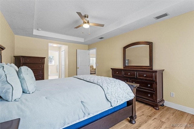 bedroom with light hardwood / wood-style floors, a tray ceiling, ceiling fan, a textured ceiling, and ensuite bathroom