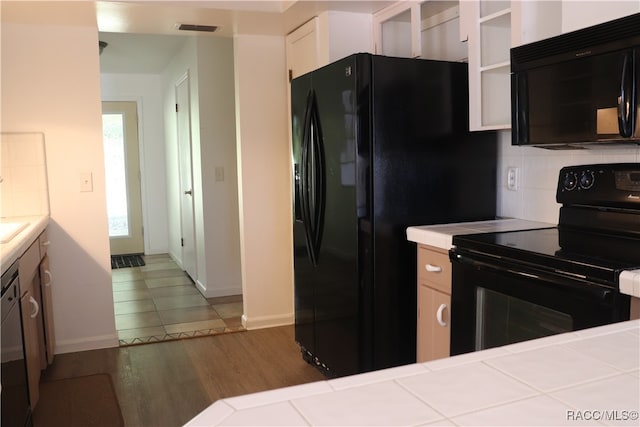 kitchen featuring white cabinetry, tile counters, backsplash, hardwood / wood-style floors, and black appliances