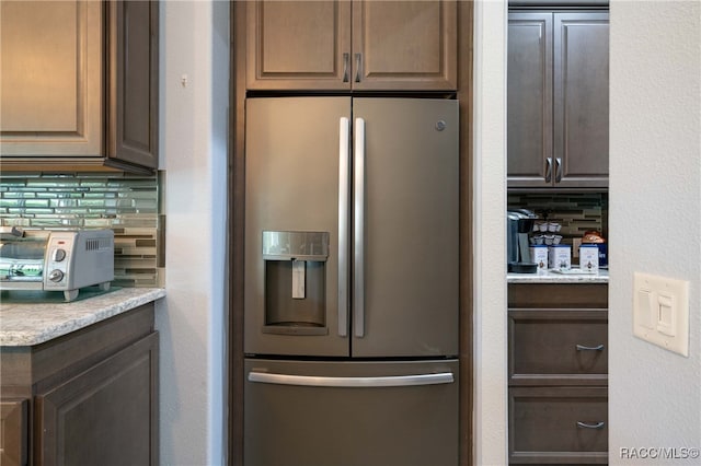 kitchen featuring backsplash, dark brown cabinets, light stone countertops, and stainless steel refrigerator with ice dispenser