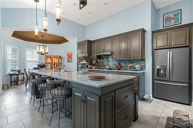 kitchen with stainless steel refrigerator with ice dispenser, backsplash, dark brown cabinets, and an island with sink