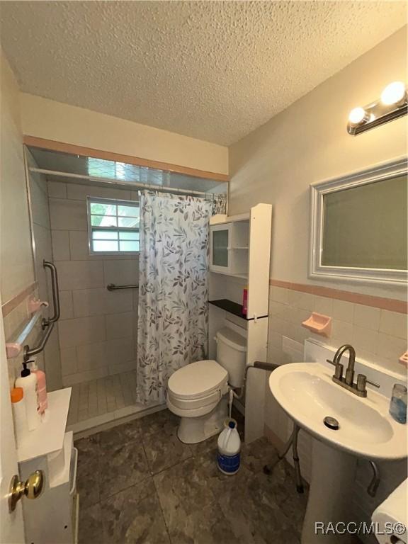 bathroom featuring sink, a shower with curtain, a textured ceiling, toilet, and tile walls