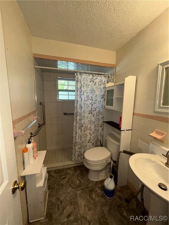 bathroom featuring a shower with shower curtain, sink, toilet, and a textured ceiling