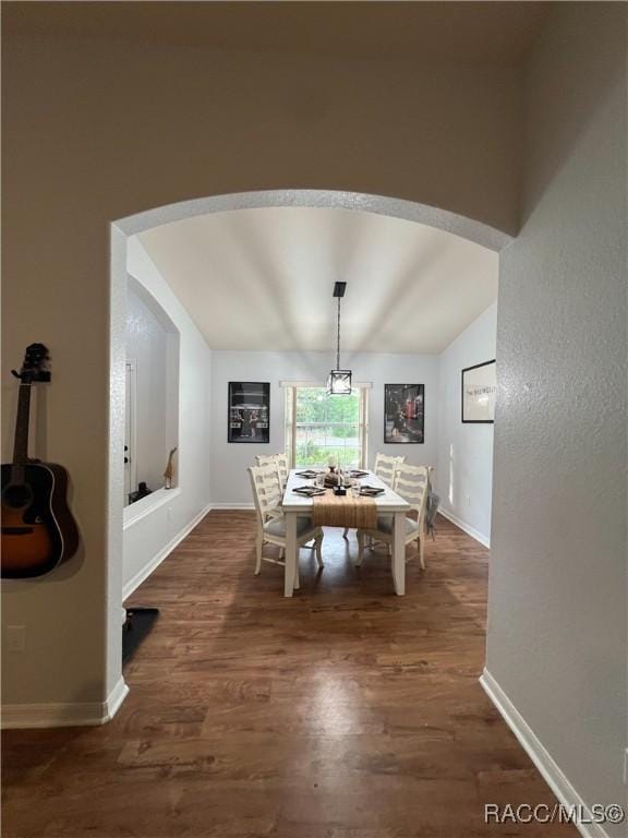 dining area featuring arched walkways, baseboards, vaulted ceiling, and dark wood-style flooring