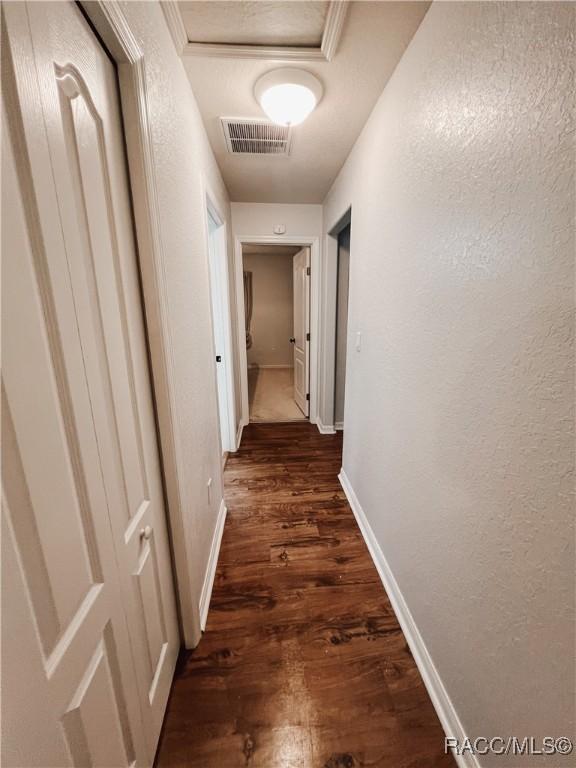 hall featuring baseboards, a textured wall, dark wood-style floors, and visible vents