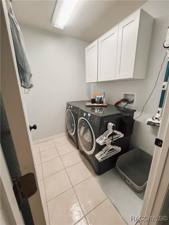 clothes washing area with cabinet space, light tile patterned floors, and washing machine and clothes dryer