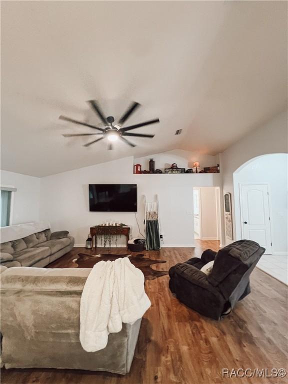 living area featuring a ceiling fan, arched walkways, wood finished floors, baseboards, and lofted ceiling