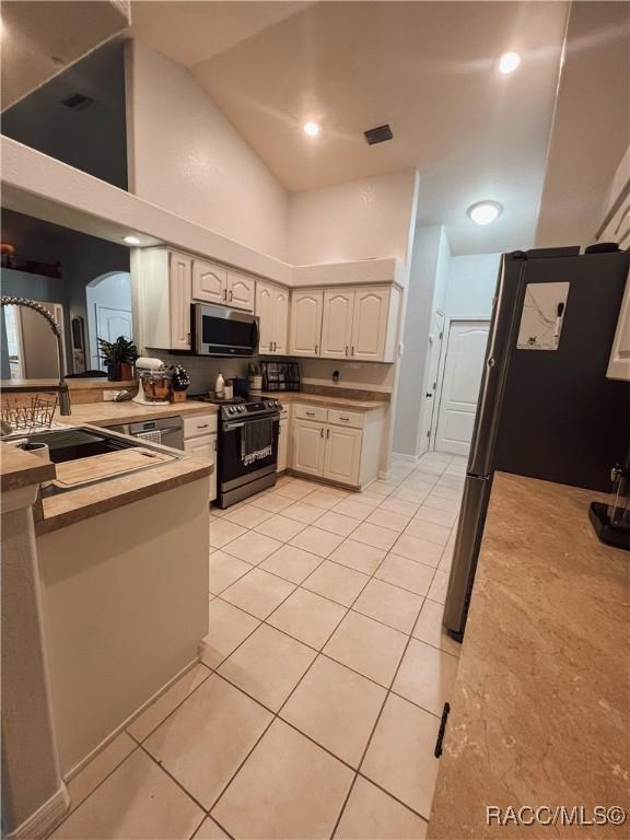 kitchen featuring arched walkways, stove, stainless steel microwave, and light tile patterned floors