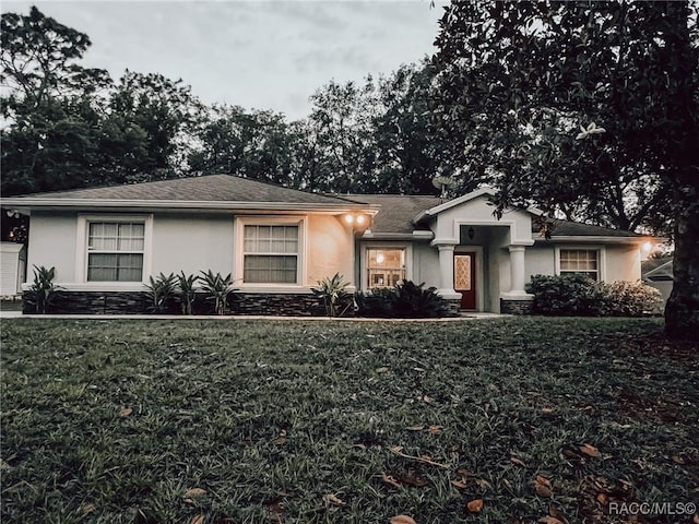 ranch-style home with a front yard, stone siding, and stucco siding