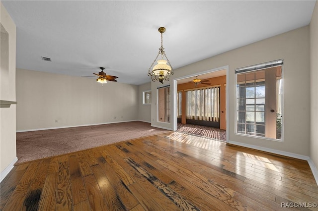 interior space with ceiling fan with notable chandelier, wood-type flooring, and visible vents