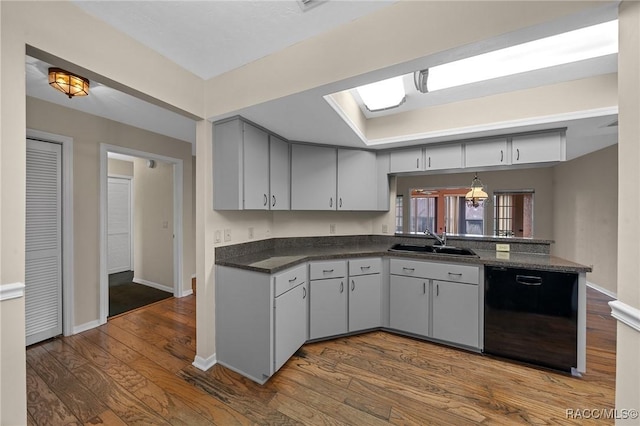 kitchen with a sink, black dishwasher, dark wood-style floors, dark countertops, and a raised ceiling