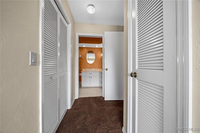 corridor featuring carpet flooring, a textured wall, and a sink