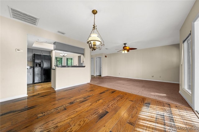 interior space with ceiling fan with notable chandelier, wood-type flooring, visible vents, and baseboards