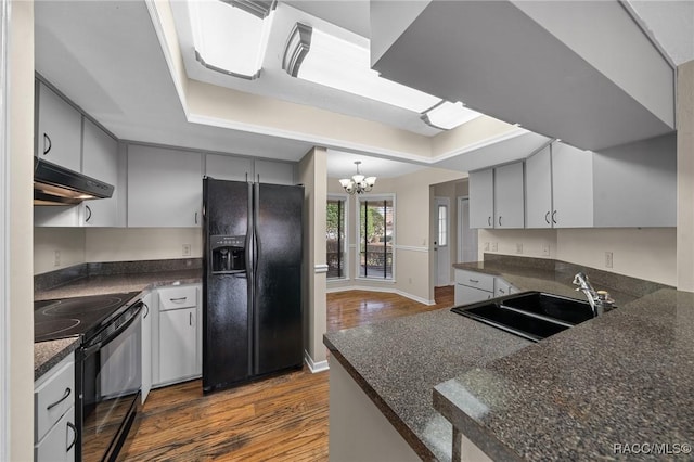 kitchen with dark countertops, black appliances, under cabinet range hood, and a sink