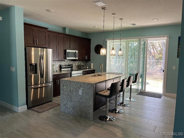 kitchen with a kitchen island with sink, light stone counters, dark brown cabinetry, and appliances with stainless steel finishes