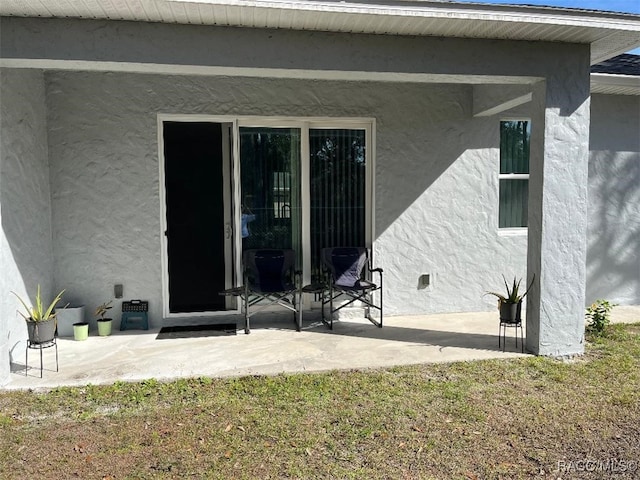 entrance to property featuring a patio area and a lawn