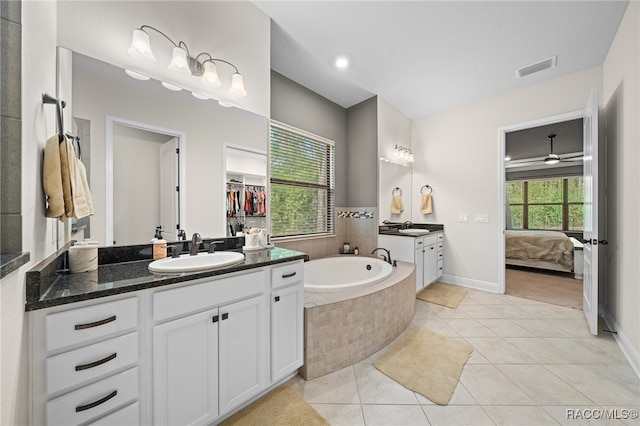 bathroom with tile patterned flooring, vanity, tiled bath, and ceiling fan