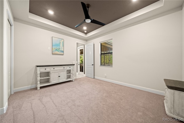 unfurnished bedroom with light colored carpet, a raised ceiling, and ceiling fan