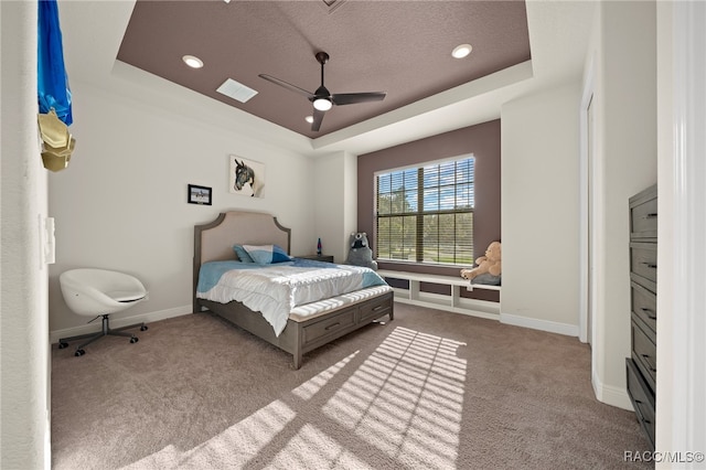 carpeted bedroom with a textured ceiling, a raised ceiling, and ceiling fan