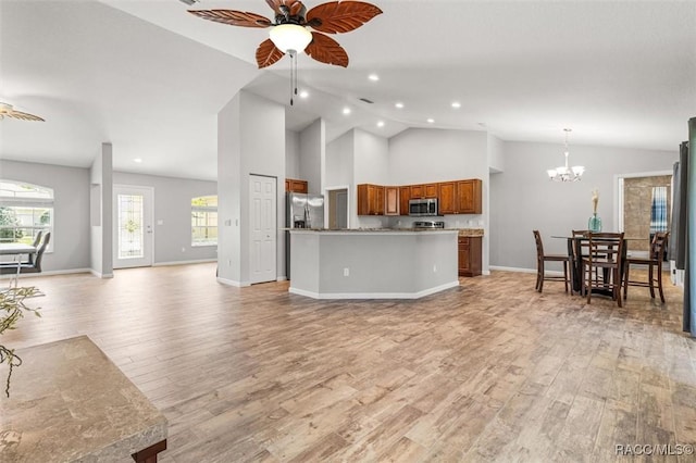 kitchen featuring brown cabinetry, light wood-style flooring, open floor plan, stainless steel appliances, and ceiling fan with notable chandelier