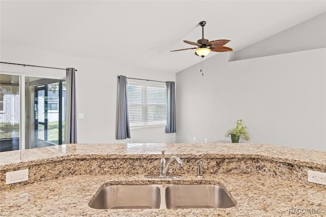 kitchen with lofted ceiling, light stone countertops, ceiling fan, and a sink