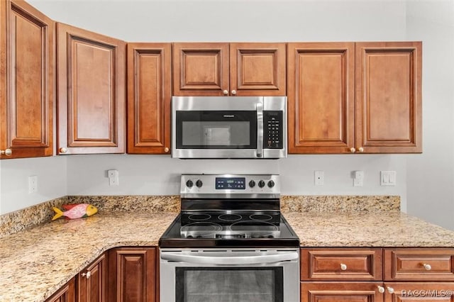 kitchen with stainless steel appliances, light stone counters, and brown cabinets