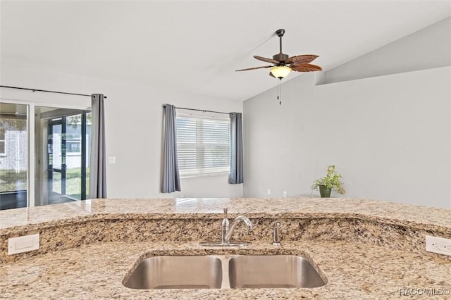 kitchen with vaulted ceiling, ceiling fan, light stone counters, and a sink