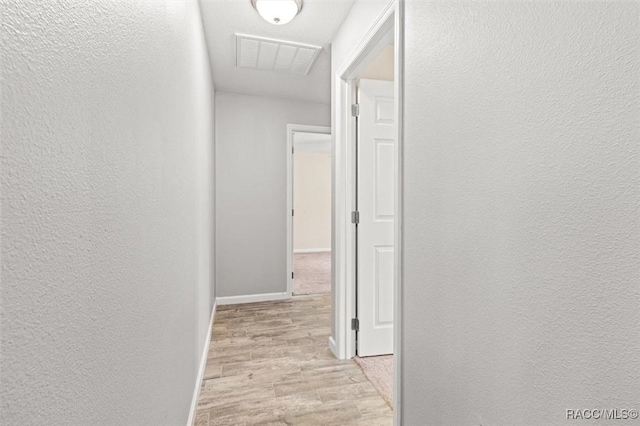 hall with light wood finished floors, baseboards, visible vents, and a textured wall