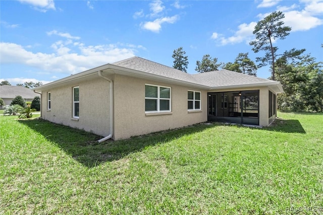 rear view of house with a sunroom, a shingled roof, stucco siding, and a yard