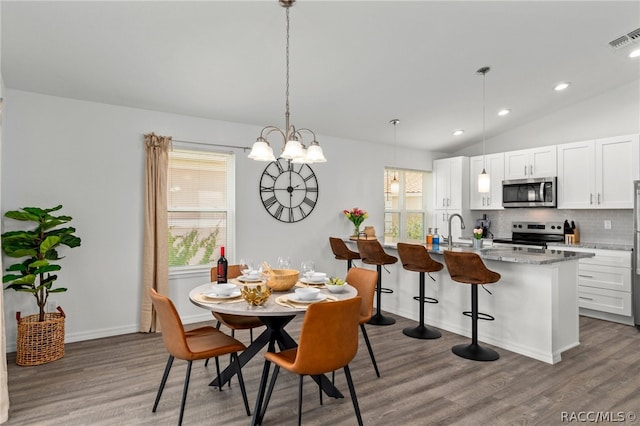 dining space with a chandelier, hardwood / wood-style floors, lofted ceiling, and sink