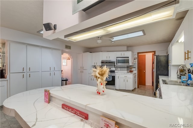 kitchen with kitchen peninsula, appliances with stainless steel finishes, backsplash, sink, and white cabinetry