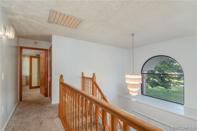 hall with light colored carpet, a textured ceiling, and an inviting chandelier