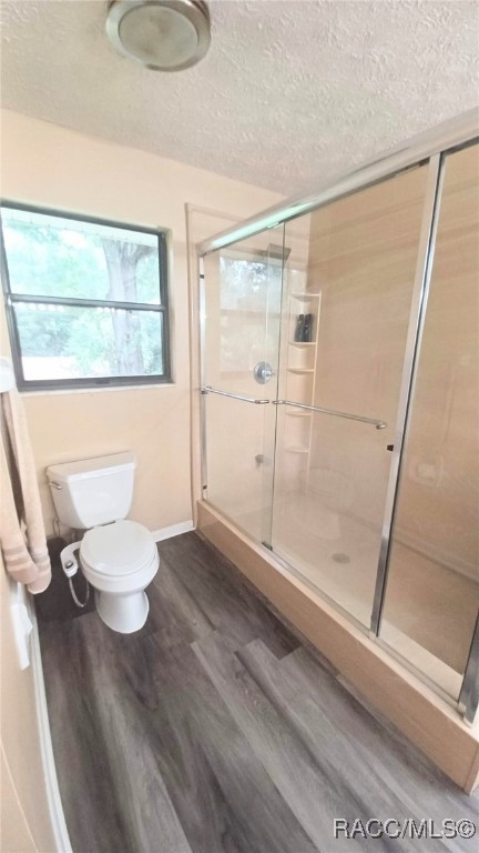 bathroom with hardwood / wood-style flooring, toilet, a shower with shower door, and a textured ceiling