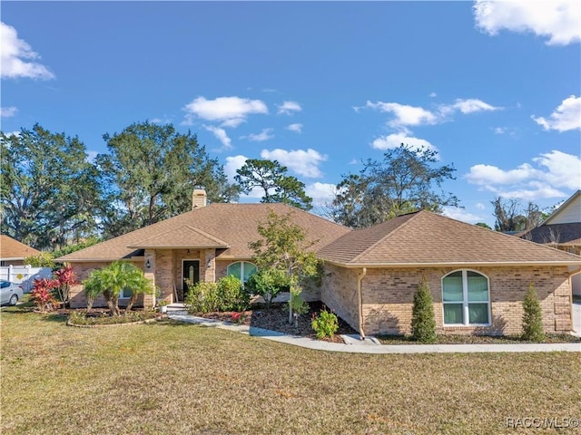 single story home featuring a chimney, roof with shingles, brick siding, and a front lawn