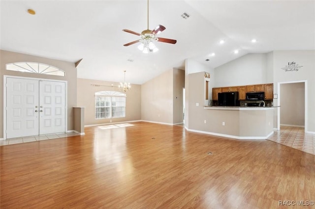 unfurnished living room featuring ceiling fan with notable chandelier, high vaulted ceiling, and light wood-type flooring