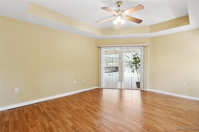 spare room with a tray ceiling, light hardwood / wood-style floors, and ceiling fan