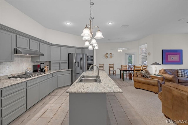 kitchen with a kitchen island with sink, under cabinet range hood, stainless steel appliances, a sink, and open floor plan