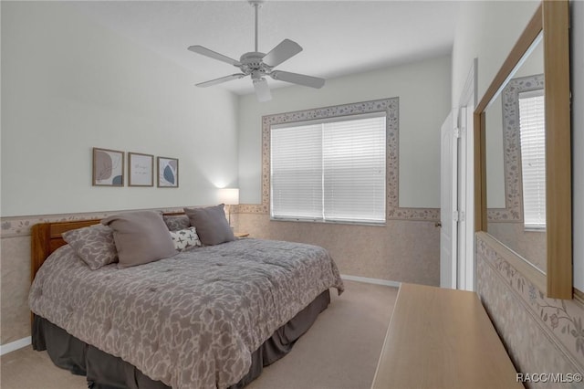 carpeted bedroom with wallpapered walls, multiple windows, a ceiling fan, and wainscoting