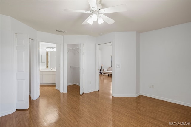 unfurnished bedroom featuring visible vents, a walk in closet, a closet, light wood-style floors, and baseboards