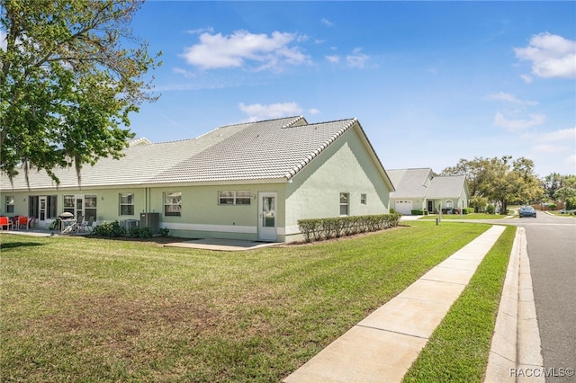 back of house featuring a lawn, a tiled roof, a patio, and stucco siding